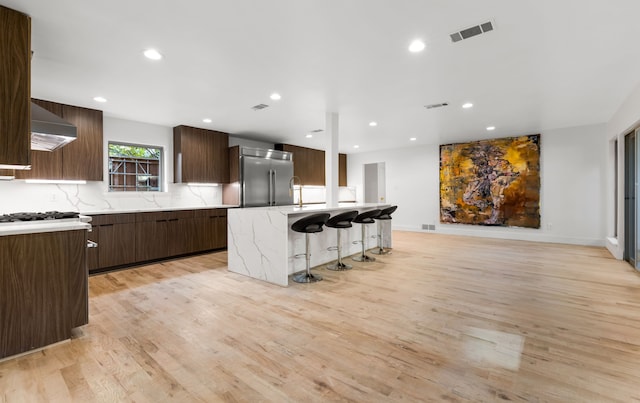 9415 Hill View Dr, Dallas, TX 75231 - kitchen with built in fridge, modern cabinets, light wood finished floors, exhaust hood, and a kitchen breakfast bar
