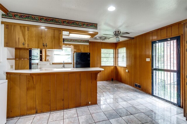 1231 Arizona Ave, Dallas, TX 75216 - kitchen with brown cabinets, a peninsula, a ceiling fan, wooden walls, and freestanding refrigerator