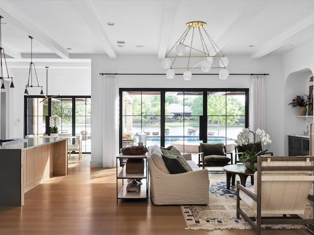 living area with beamed ceiling, light wood-type flooring, a chandelier, and arched walkways