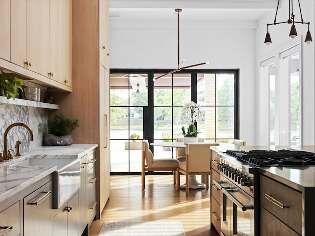 kitchen featuring high end stainless steel range, light wood-type flooring, a sink, decorative backsplash, and pendant lighting