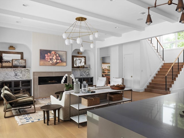 living area with a fireplace, beam ceiling, stairs, wood finished floors, and a chandelier