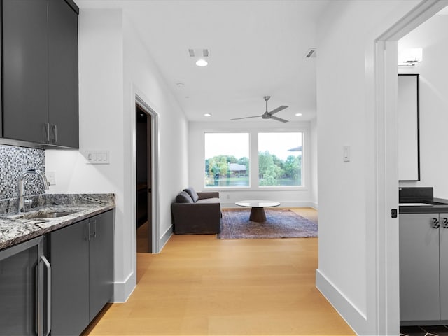 hallway featuring a sink, light wood-type flooring, baseboards, beverage cooler, and recessed lighting
