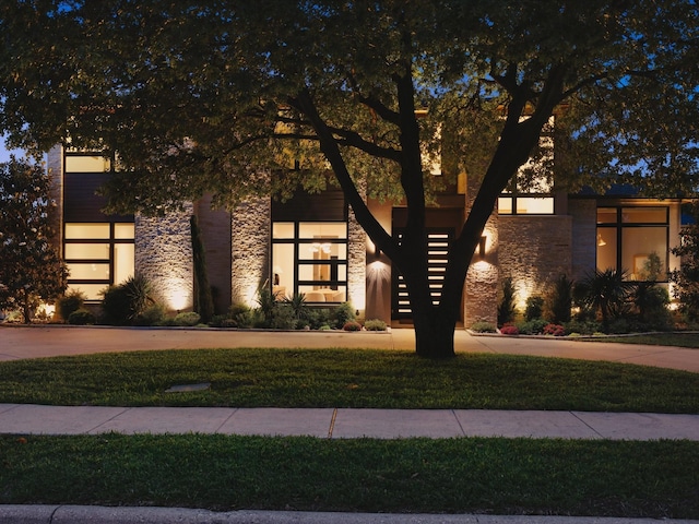 view of front facade with stone siding, curved driveway, stairway, and a front lawn