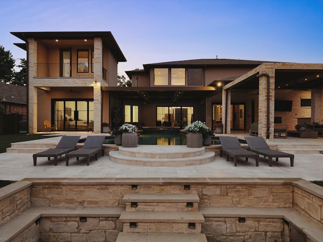 back of house at dusk featuring a balcony, ceiling fan, a patio, an outdoor pool, and french doors
