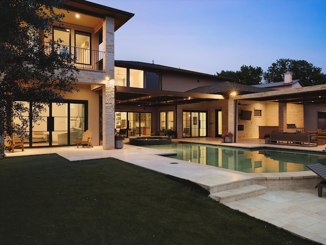 back of property featuring a patio area, a balcony, a pool with connected hot tub, a chimney, and a yard