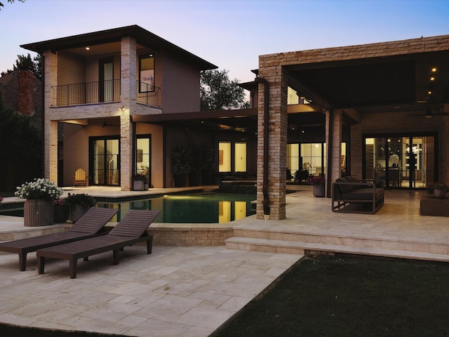 back of property at dusk with a balcony, a patio, and an outdoor pool