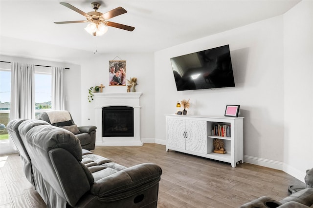 3008 Aransas Ave, Aubrey, TX 76227 - living area featuring a glass covered fireplace, wood finished floors, ceiling fan, and baseboards