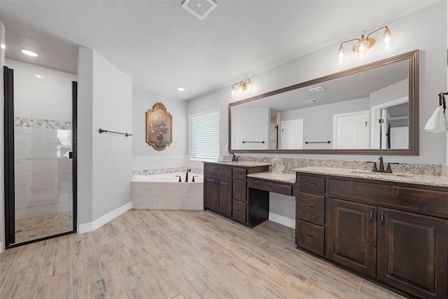 full bathroom featuring a garden tub, wood finished floors, vanity, tiled shower, and a textured ceiling