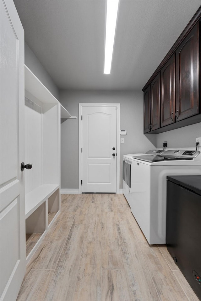 clothes washing area featuring washing machine and clothes dryer, cabinet space, light wood-style floors, and baseboards