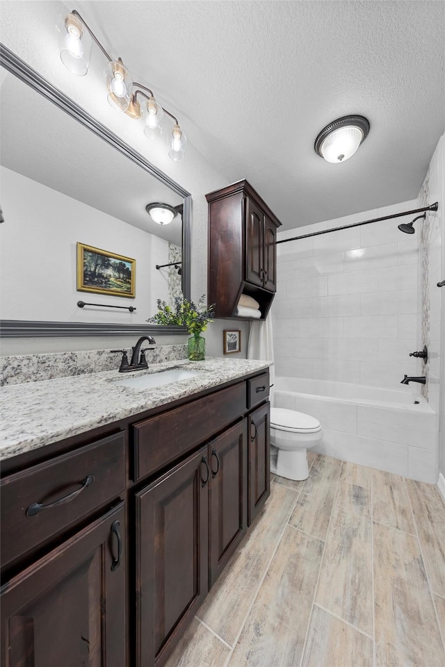 full bathroom featuring wood finished floors, toilet, vanity, a textured ceiling, and tub / shower combination