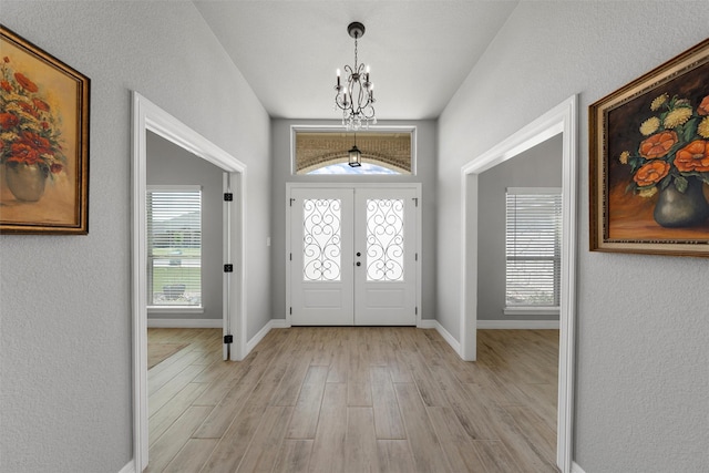 entrance foyer featuring a chandelier, light wood-type flooring, baseboards, a textured wall, and french doors