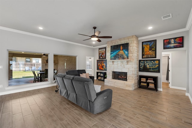 living area with a ceiling fan, baseboards, crown molding, a stone fireplace, and wood finished floors