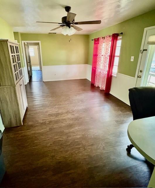 2142 Woodard St, Abilene, TX 79605 - unfurnished living room featuring a ceiling fan, healthy amount of natural light, dark wood-style floors, and a wainscoted wall