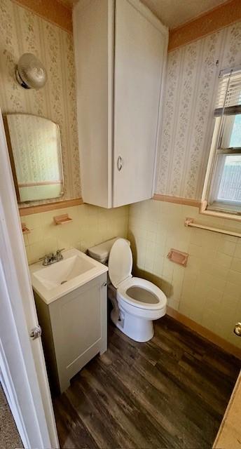 2142 Woodard St, Abilene, TX 79605 - bathroom featuring wallpapered walls, toilet, vanity, wood finished floors, and wainscoting