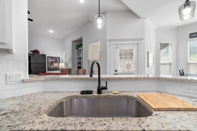 kitchen with a sink, light stone countertops, white cabinetry, open floor plan, and decorative light fixtures