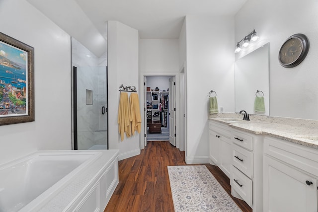 full bath featuring a shower stall, wood finished floors, a spacious closet, vanity, and a garden tub
