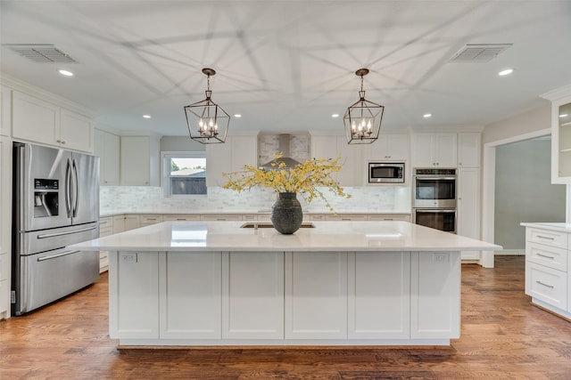 kitchen featuring appliances with stainless steel finishes, a chandelier, wall chimney range hood, light countertops, and recessed lighting