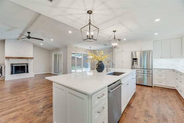 kitchen featuring appliances with stainless steel finishes, a sink, a ceiling fan, an island with sink, and wood finished floors