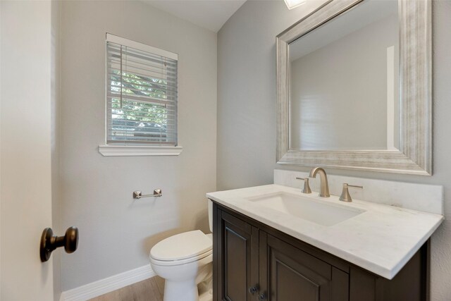bathroom with toilet, vanity, baseboards, and wood finished floors