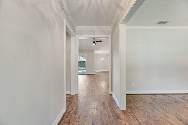 corridor with wood finished floors, ornamental molding, and baseboards