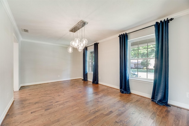 spare room featuring a chandelier, wood finished floors, crown molding, and baseboards