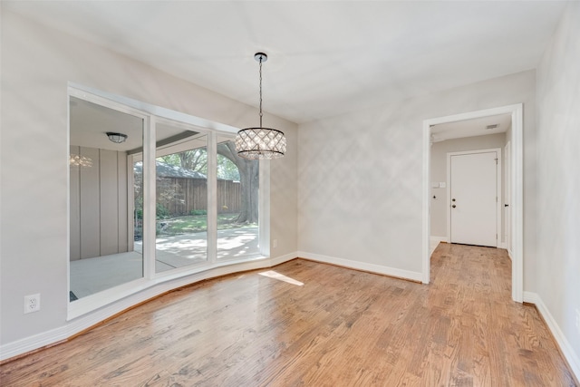 unfurnished dining area with a chandelier, wood finished floors, and baseboards