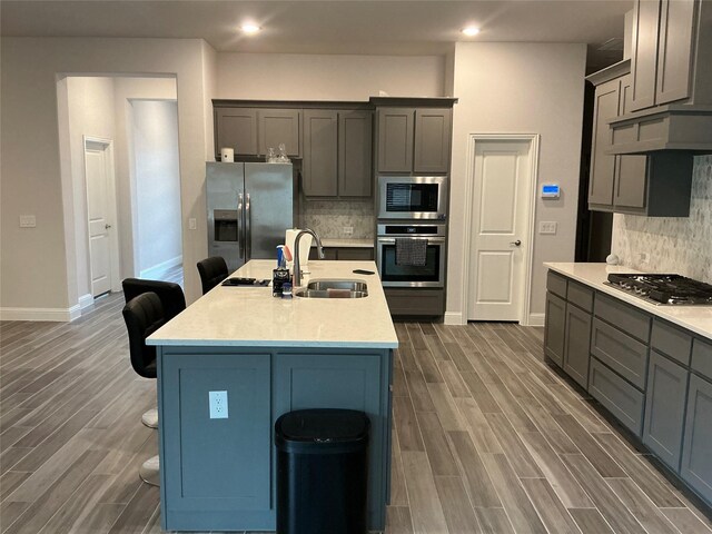 kitchen with appliances with stainless steel finishes, a sink, baseboards, a breakfast bar, and light countertops