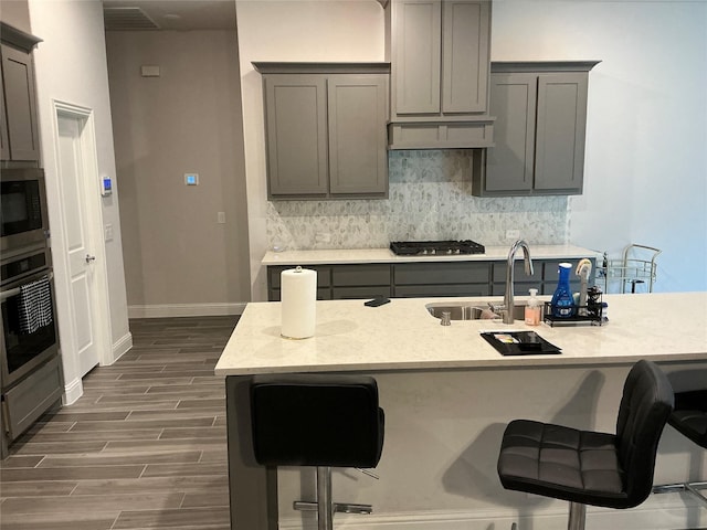 kitchen with gray cabinetry, stainless steel appliances, backsplash, dark wood-type flooring, and a breakfast bar