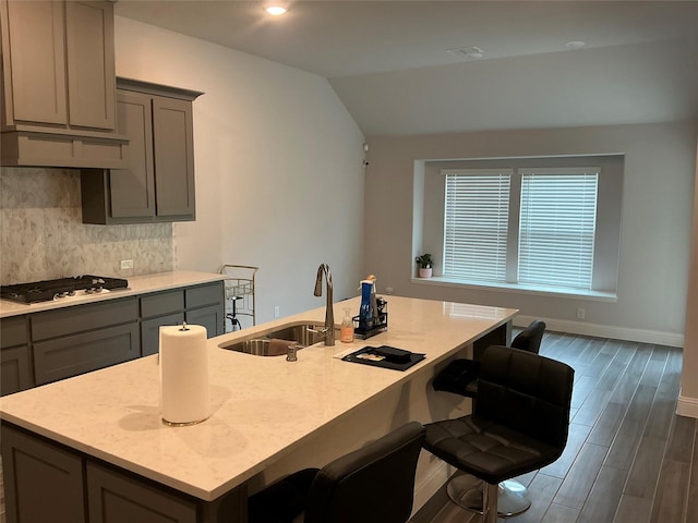 kitchen with gray cabinets, gas cooktop, a sink, tasteful backsplash, and dark wood-type flooring