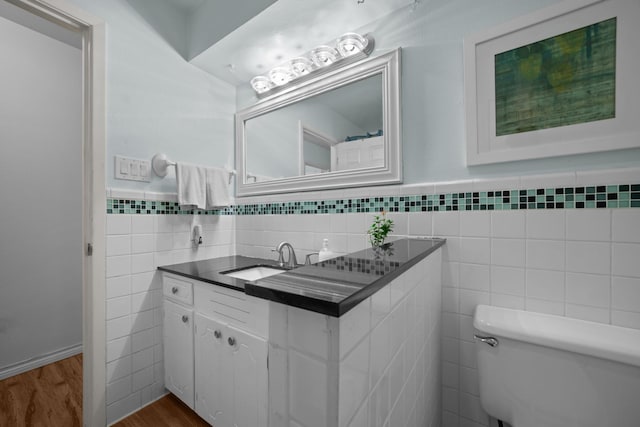 bathroom featuring tile walls, wood finished floors, toilet, vanity, and wainscoting