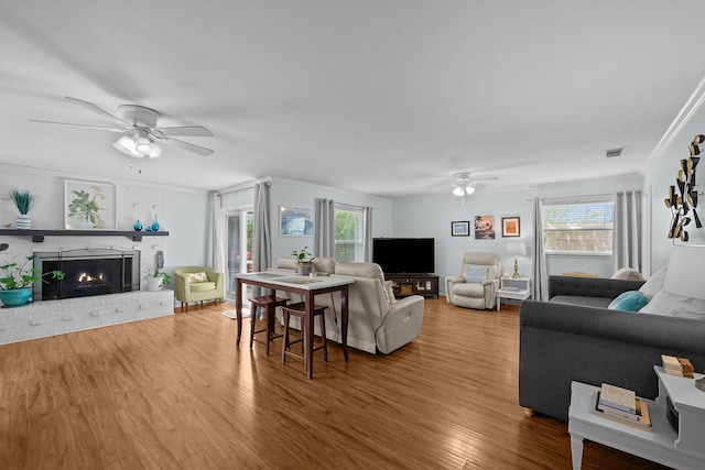 living area featuring ceiling fan, crown molding, wood finished floors, and a brick fireplace