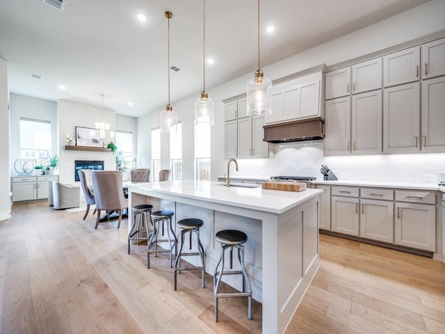 4208 Sunrise Ln, Celina, TX 75078 - kitchen with gray cabinets, a sink, decorative backsplash, a breakfast bar area, and light wood finished floors