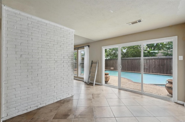 unfurnished room featuring brick wall, tile patterned floors, and a textured ceiling
