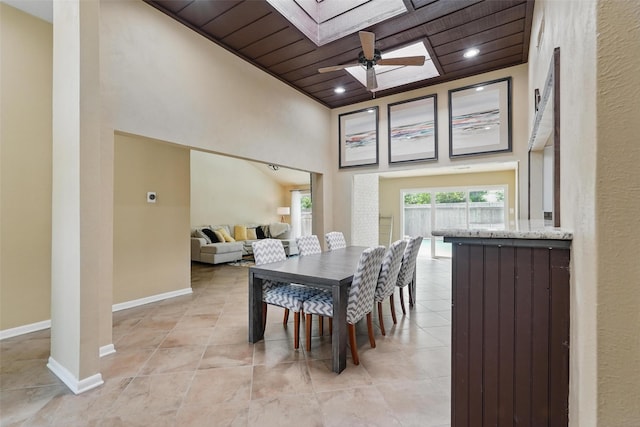 dining space featuring a skylight, wood ceiling, light tile patterned flooring, baseboards, and a towering ceiling