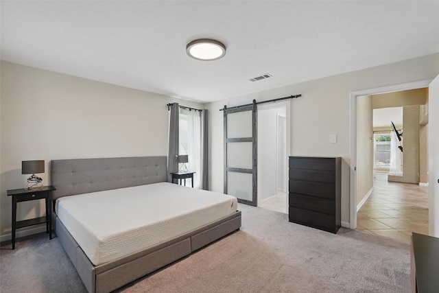 bedroom featuring light colored carpet, a barn door, baseboards, and light tile patterned floors