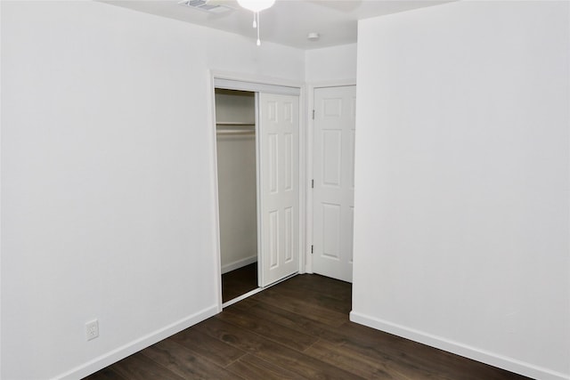 unfurnished bedroom with dark wood-type flooring, baseboards, a closet, and a ceiling fan