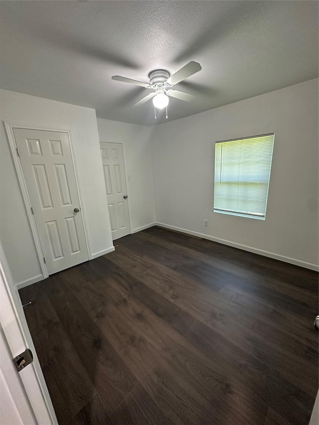 unfurnished bedroom featuring dark wood-type flooring, baseboards, ceiling fan, and a textured ceiling