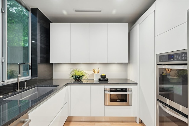 957 Easton Pl, Dallas, TX 75218 - kitchen with a sink, appliances with stainless steel finishes, white cabinetry, dark stone counters, and modern cabinets