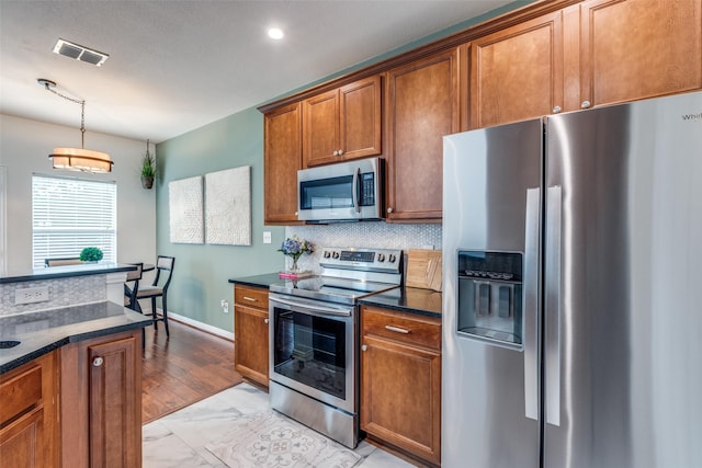 kitchen featuring appliances with stainless steel finishes, light marble finish floors, backsplash, brown cabinetry, and decorative light fixtures