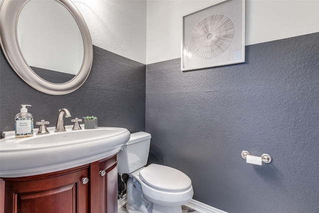 bathroom featuring toilet, a textured wall, and vanity