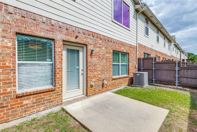 property entrance with a patio area, central air condition unit, fence, and brick siding