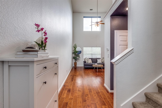 entryway featuring light wood-style flooring, a ceiling fan, a towering ceiling, stairway, and baseboards