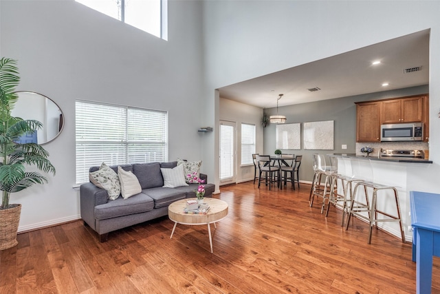 living area with a high ceiling, light wood-type flooring, baseboards, and recessed lighting
