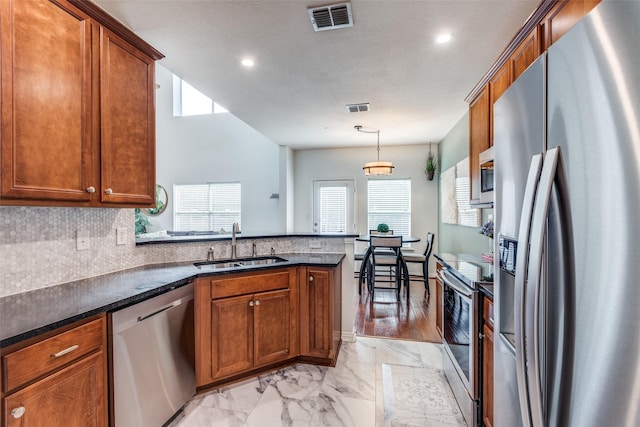 kitchen with stainless steel appliances, a sink, a peninsula, light marble finish floors, and brown cabinetry