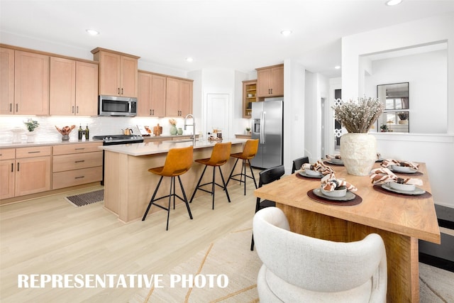 kitchen featuring stainless steel appliances, light brown cabinetry, a breakfast bar, backsplash, and recessed lighting