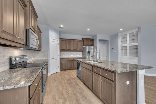 516 Smart Strike Trl, Granbury, TX 76049 - kitchen with stainless steel appliances, a sink, light wood-style floors, a center island with sink, and tasteful backsplash