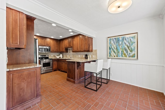 7609 Spring Valley Rd, Dallas, TX 75254 - kitchen featuring stainless steel appliances, brick patterned flooring, a breakfast bar area, brown cabinets, and a peninsula