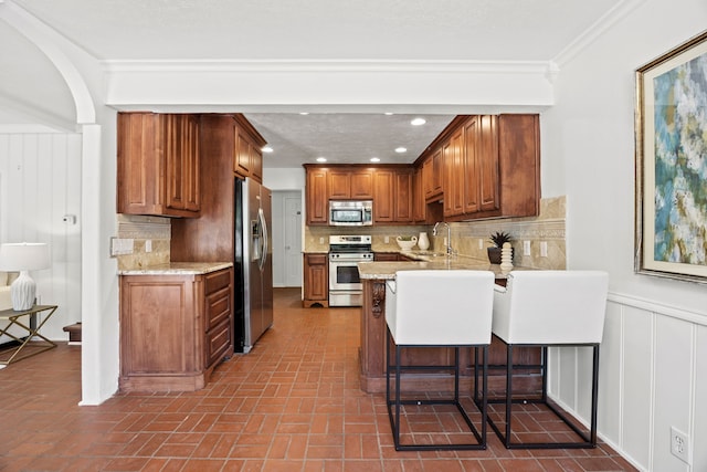 7609 Spring Valley Rd, Dallas, TX 75254 - kitchen with appliances with stainless steel finishes, a sink, a peninsula, brown cabinetry, and crown molding
