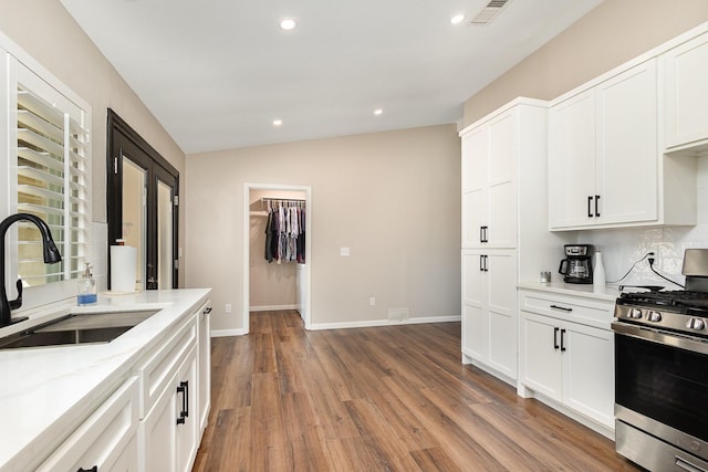 3105 Kensington Dr, Mesquite, TX 75150 - kitchen featuring stainless steel gas stove, a sink, vaulted ceiling, light wood finished floors, and white cabinets