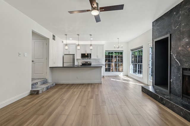 7525 Holly Hill Dr Unit 17, Dallas, TX 75231 - unfurnished living room with light wood finished floors, baseboards, a ceiling fan, a chandelier, and a high end fireplace